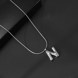 Macro-opname van 3D-letter N hanger met gladde slangenketting op zwarte achtergrond