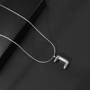 Detailopname van de zilveren bubble letter J hanger aan een gladde slangenketting