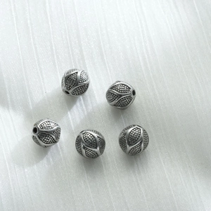 Primo piano di cinque perline distanziatrici vintage in acciaio inox con motivi a rilievo