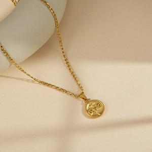 Macro detail of Aries zodiac gold circular relief pendant and Figaro chain links