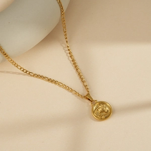 Close-up of gold stainless steel Figaro chain necklace with round zodiac pendant