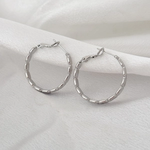 Macro shot of silver geometric hoop earrings with textured chain link design on white velvet