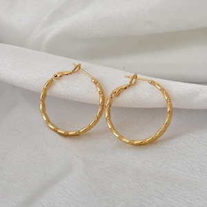 Detail of gold bamboo texture hoop earrings on white silk fabric with secure clasp
