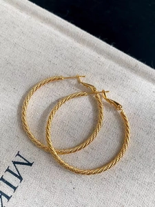 Macro detail of large gold twisted rope hoop earrings resting on a canvas background