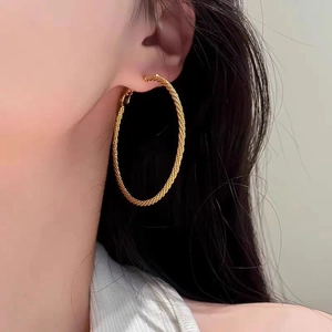 Detail of large gold hoop earrings featuring a twisted rope texture worn by a model