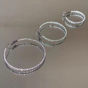 Three sizes of silver twisted hoop earrings displayed on a reflective mirror surface