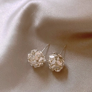 Macro shot of silver woven sequin ball stud earrings on champagne silk fabric