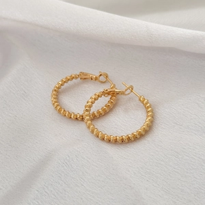 Boucles d'oreilles créoles torsadées dorées style vintage français sur tissu blanc