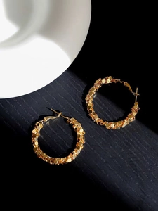 Detail of gold layered hoop earrings with textured glitter finish on wood