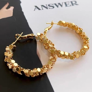 Detail of gold geometric hoop earrings with layered hexagonal metal flakes on magazine