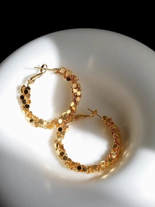 Close-up of golden hoop earrings with shimmering scale texture on a ceramic dish