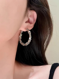 Close-up of sparkling silver hoop earrings with stacked metal discs texture on a model