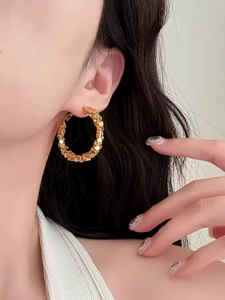 Macro detail of large gold hoop earrings with shimmering textured sequin-style metal scales
