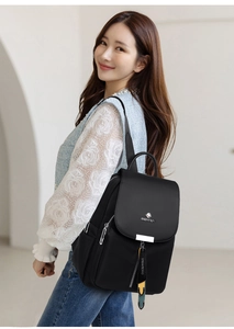Détail d'un sac à dos noir en nylon imperméable avec logo argenté porté par une femme sur le côté