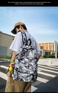 Outdoor shot of black and white manga print backpack with a green dinosaur plush keychain