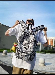 Outdoor view of a black and white comic print backpack with a green dinosaur plush charm