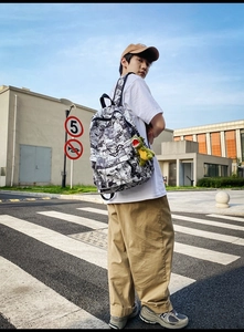 Outdoor street view of a comic print backpack with a green dinosaur plush keychain