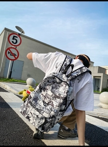Detail of stylish manga print backpack featuring a cute yellow dinosaur plush pendant