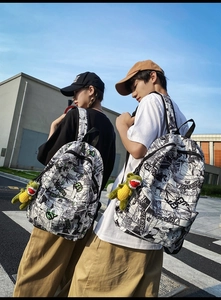 Close-up of urban graffiti backpack with green embroidery and cute dinosaur plush toy charm