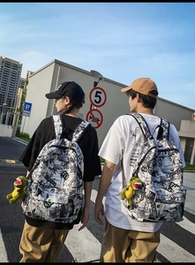 Close-up of street style backpack with black and white manga print and green dinosaur charm