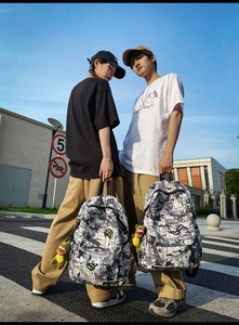 Close-up of black and white comic print backpack with fly outride text and dinosaur charm