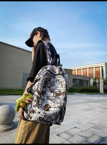Detail of trendy comic print backpack with a cute green dinosaur plush keychain accessory