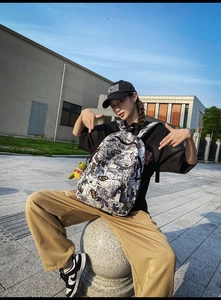 Outdoor lifestyle shot of a graffiti print backpack with a green dinosaur keychain charm