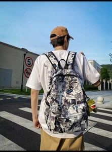 Outdoor street view of a large comic print backpack with a green dinosaur plush charm