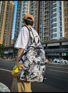 Street view of a white canvas backpack with anime print and a green dinosaur pendant