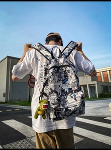 Detail of urban fashion backpack with manga print and green dinosaur plush charm