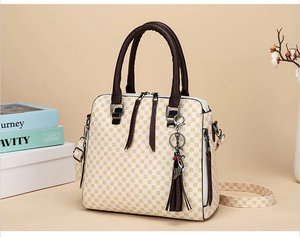 Detail of white handbag with yellow geometric print featuring brown tassels and cat charm