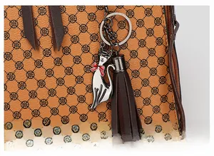Detail of printed leather bag featuring a cat metal charm and brown leather tassel