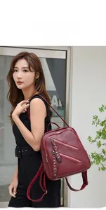 Detail of wine red PU leather backpack with silver zippers and rivets on female model