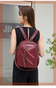 Detailed view of burgundy PU leather backpack with silver zippers and rivet accents on model