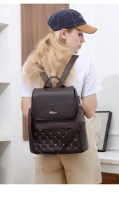 Detail of dark brown leather backpack featuring quilted pattern and gold stud accents
