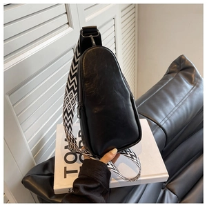 Detail of black faux leather chest bag with geometric pattern strap on white book
