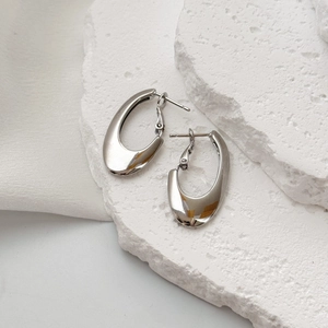 Chic silver minimalist oval hoop earrings on textured white stone background
