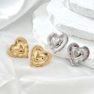 Exaggerated 18K gold and silver geometric heart stud earrings on a white stone pedestal