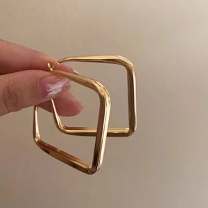 Detail of hand holding large gold geometric square hoop earrings for women