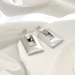 Détail de boucles d'oreilles rectangulaires argentées sur pierre blanche et soie