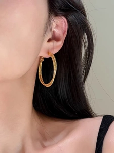 Dettaglio di orecchini a cerchio intrecciati in oro 18K con texture fine indossati