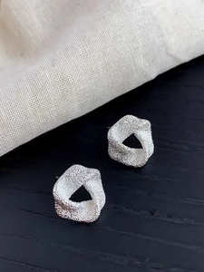 Gros plan de boucles d'oreilles carrées argentées avec une finition sablée mate texturée