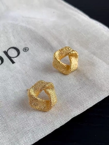Vue macro de boucles d'oreilles dorées géométriques torsadées avec texture martelée