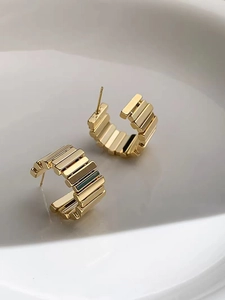 Detailed view of golden C-shaped hoop earrings with geometric step textures on white tray