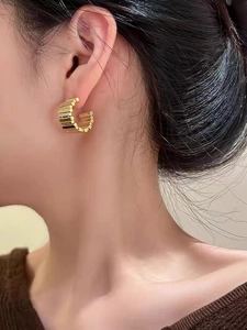 Detail of gold C-shaped hoop earrings with vertical textured stripes on model's ear