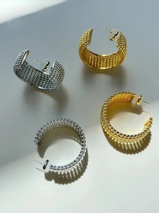 Détail de créoles en forme de C en or et argent avec surface texturée à micro-billes