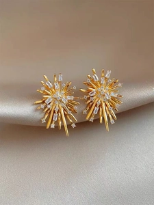 Macro view of gold firework stud earrings with sparkling cubic zirconia on silk fabric