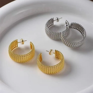 Créoles en forme de C texturées or et argent avec motif perlé tissé sur un plateau en céramique