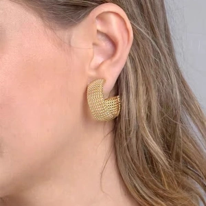 Boucles d'oreilles créoles dorées en C avec texture perlée portées par un mannequin