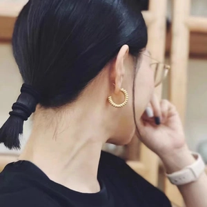 Orecchini a cerchio dorati a forma di C con trama a perline indossati da una modella
